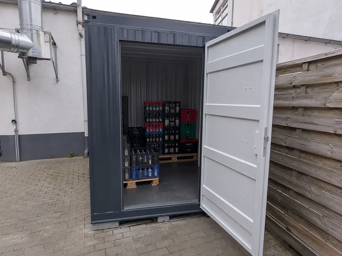 Neuer Lagercontainer mit Getränkekisten und Leergut hinter einem Gastronomiebetrieb