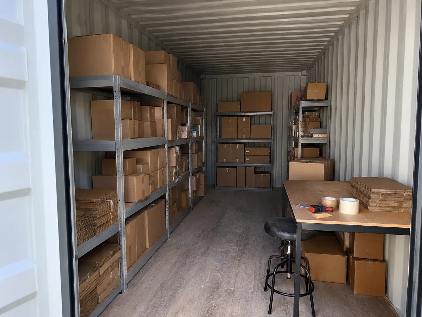 Innenraum eines Lagercontainers mit Versandregalen und kleinem Packtisch
